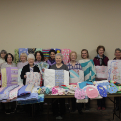 Women from the H.O.P.E. Group holding handmade quilts and blankets